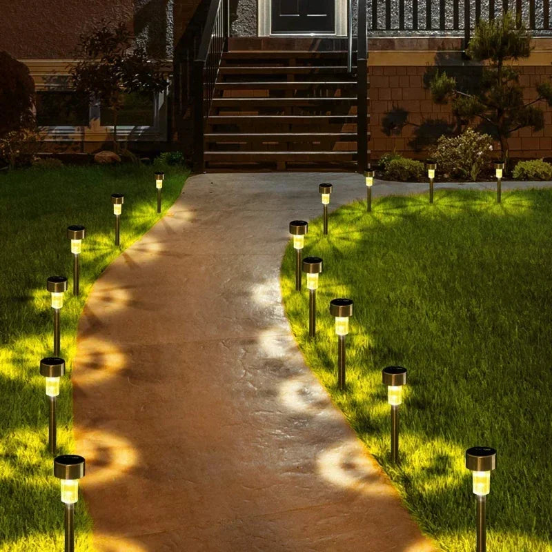 A pathway lined with solar powered garden lantern lights leading toward a house entrance.