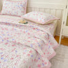 Pink and white floral quilted bedspread with pink trim and a matching pillow on a bed.