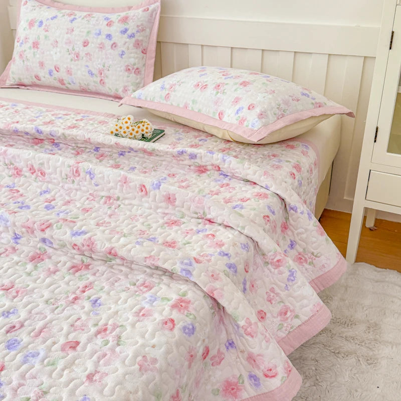 Pink and white floral quilted bedspread with pink trim and a matching pillow on a bed.
