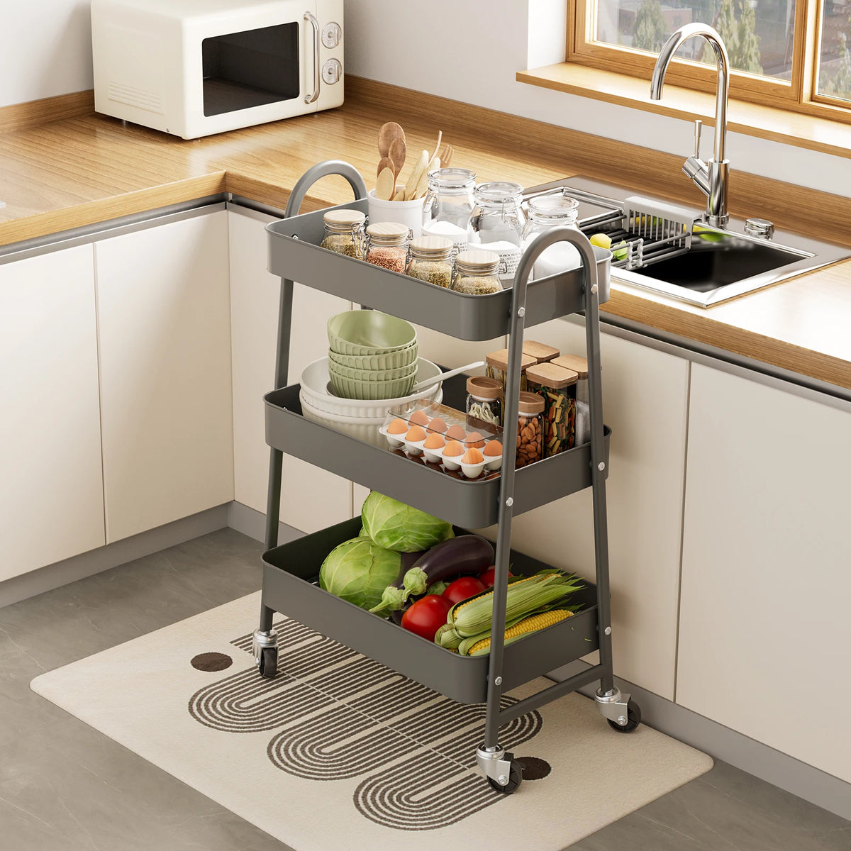 A 3-tier rolling metal storage cart filled with various kitchen items like jars and produce on a countertop.