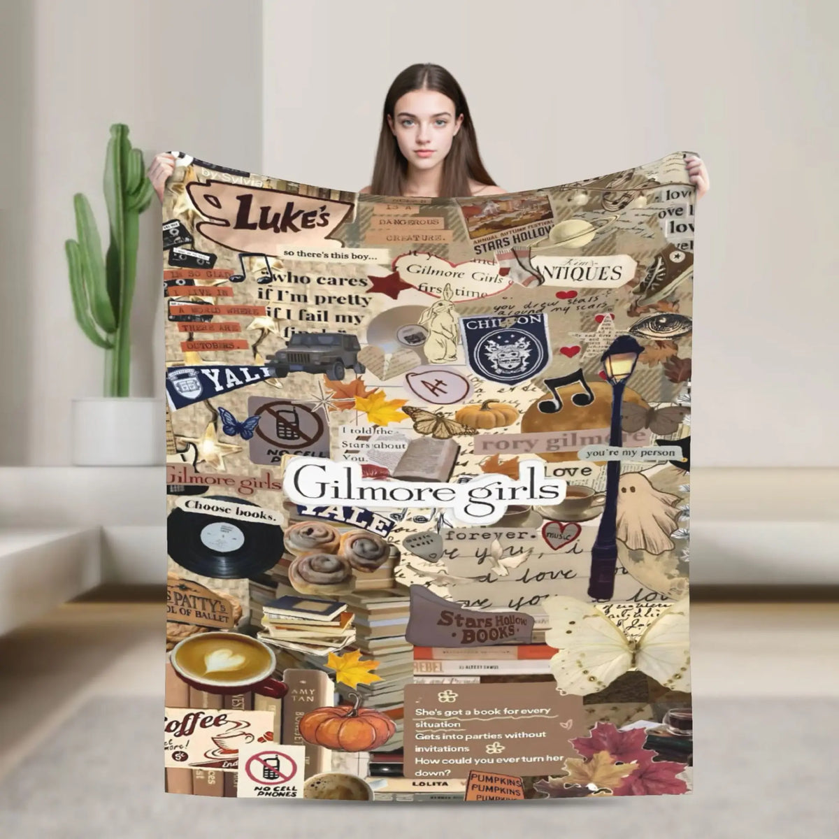 A woman holds up a large throw blanket featuring various Gilmore Girls themed graphics and text.