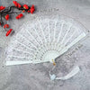White lace-trimmed folding hand fan with a golden edge displayed on a gray surface.