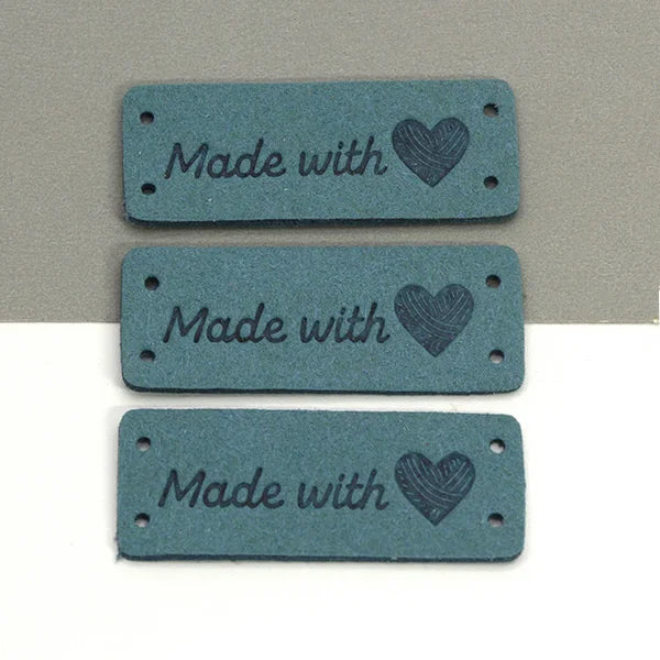 Three rectangular teal leather labels with the text Made with and a heart design.