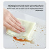 A hand wipes an oil stain off a surface using a white absorbent cloth, demonstrating waterproof and stain-proof properties.