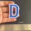 A hand holds a blue embroidered letter D patch, measuring 5 by 3.5 centimeters.