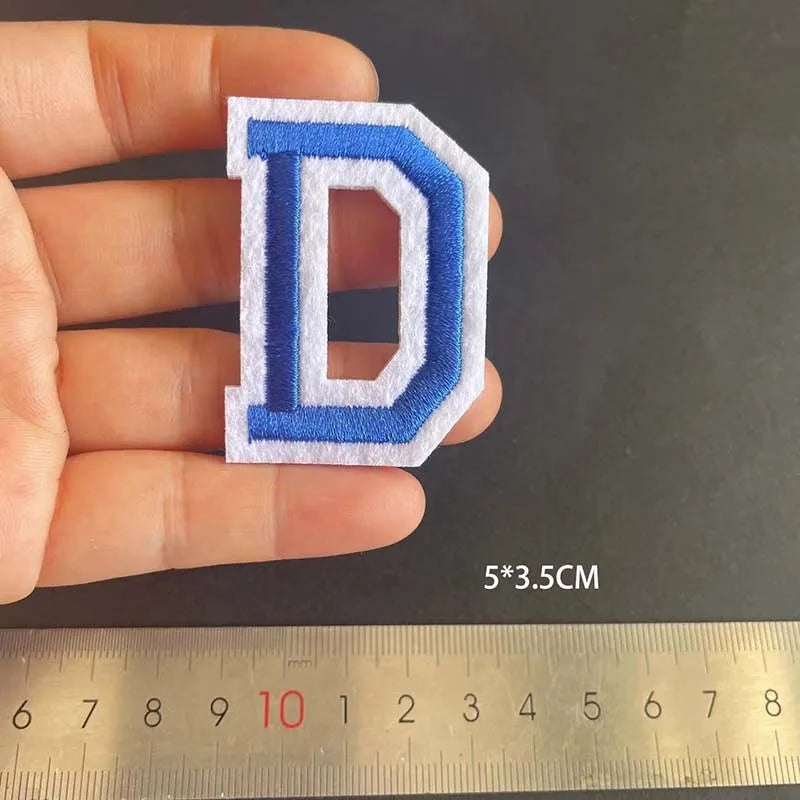 A hand holds a blue embroidered letter D patch, measuring 5 by 3.5 centimeters.