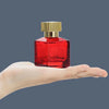 A clear red glass perfume bottle with a gold cap is held in a person's hand.