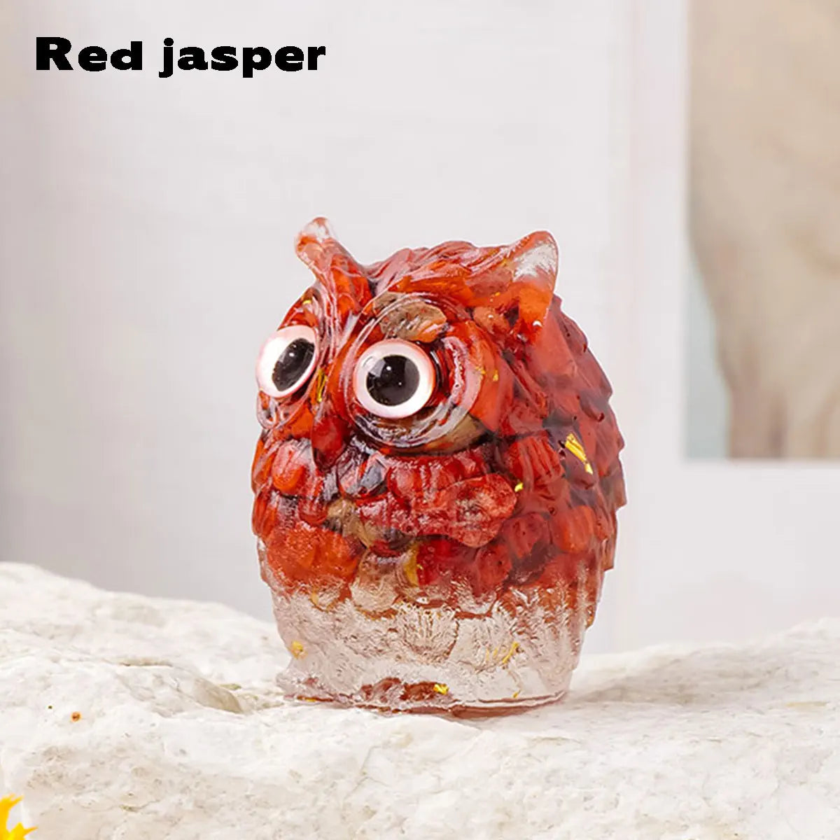 A handcrafted red jasper crystal owl figurine with large eyes sitting on a light surface.