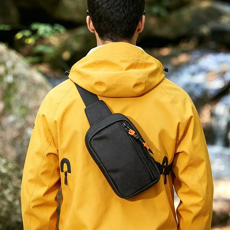 A person wearing a yellow jacket is carrying a black sling bag on their back in an outdoor setting.