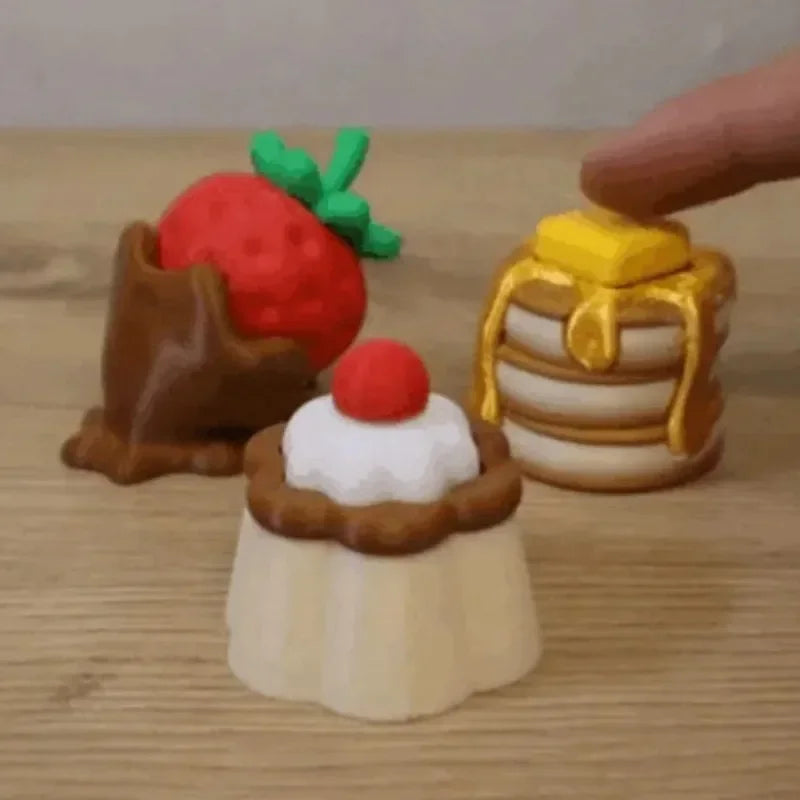 A hand is placing a strawberry, a cake, and a gold bar onto a wooden surface.