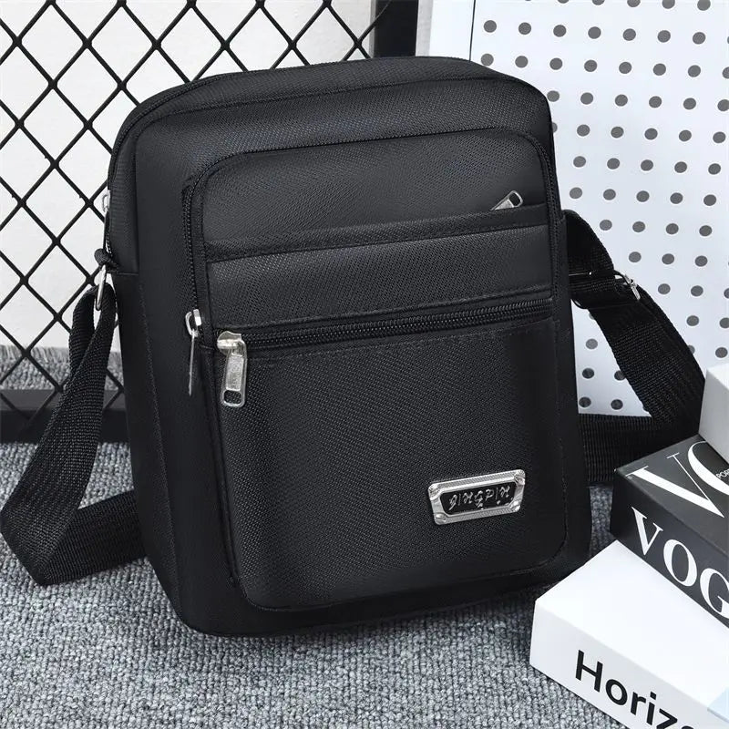 Black water-resistant multi-pocket crossbody chest bag with a strap resting on a gray surface.