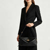 A woman wearing a black blazer and trousers holds a black genuine leather square crossbody bag with a gold lock.