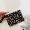 A black leopard print cosmetic bag with a zipper is held in a hand on a white surface.
