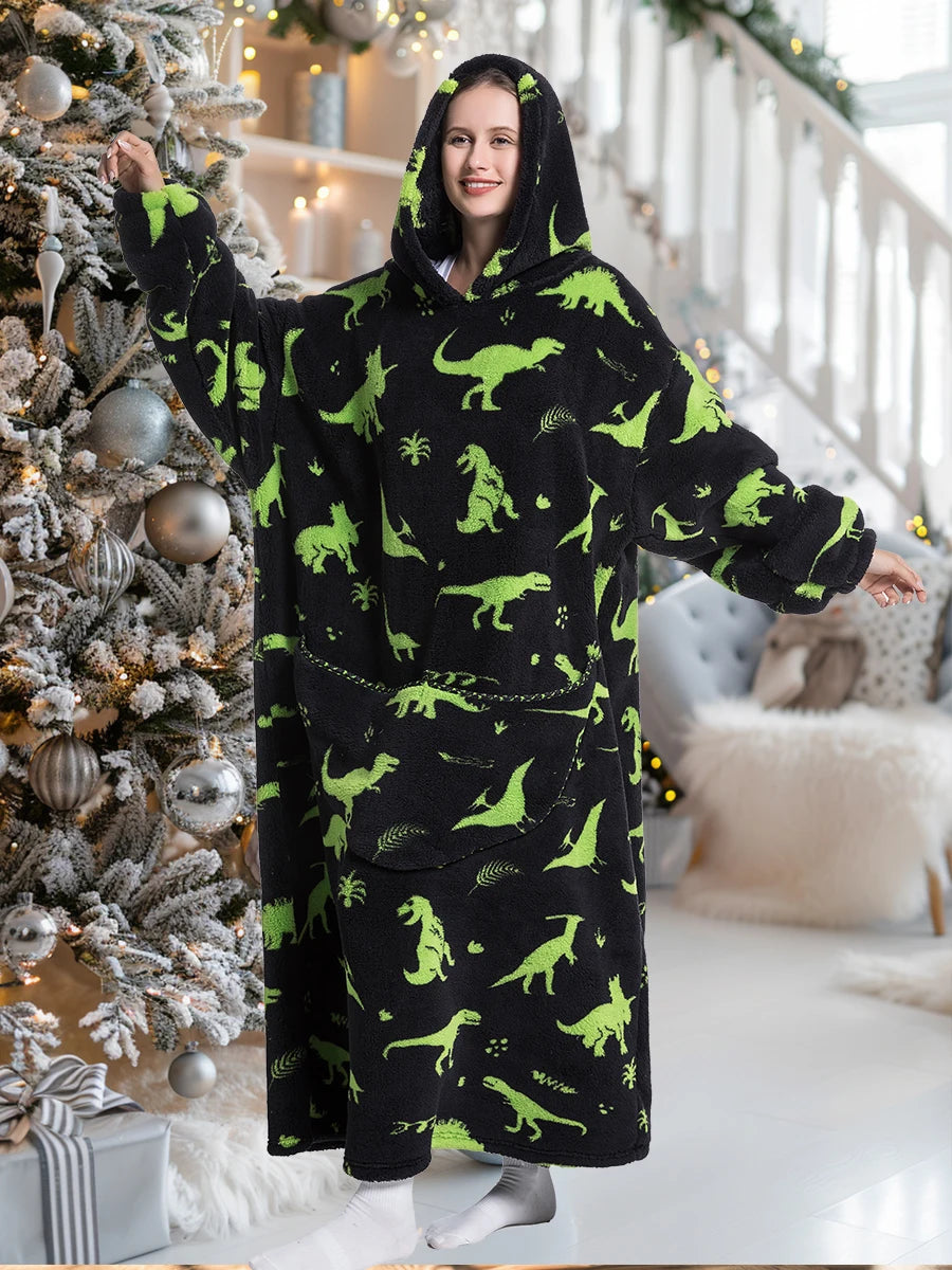 A woman wearing an oversized black hoodie blanket with green dinosaur print in a brightly lit interior.