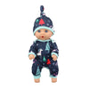 A baby doll wearing a dark blue jumpsuit outfit decorated with Christmas trees and snowflakes.
