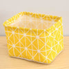 A bright yellow cotton and linen storage basket with a geometric pattern sits on a wooden surface.