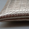 Close-up of an elegant crocodile-embossed PU leather envelope clutch in a metallic champagne color.