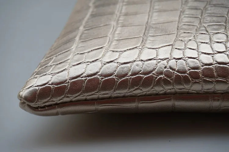 Close-up of an elegant crocodile-embossed PU leather envelope clutch in a metallic champagne color.
