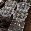 A collection of clear plastic storage organizers holding various hardware and small parts on a wooden surface.