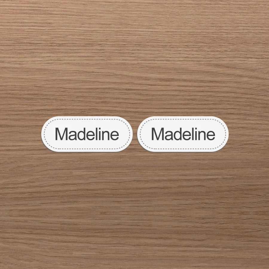 Dos etiquetas ovalas blancas con el nombre Madeline impreso sobre un fondo de madera marrón claro.