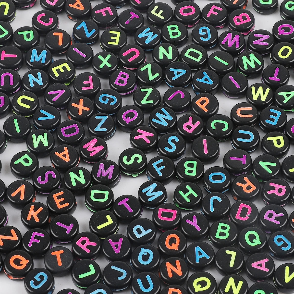 A close-up view of numerous black and colorful acrylic alphabet letter beads scattered on a white surface.