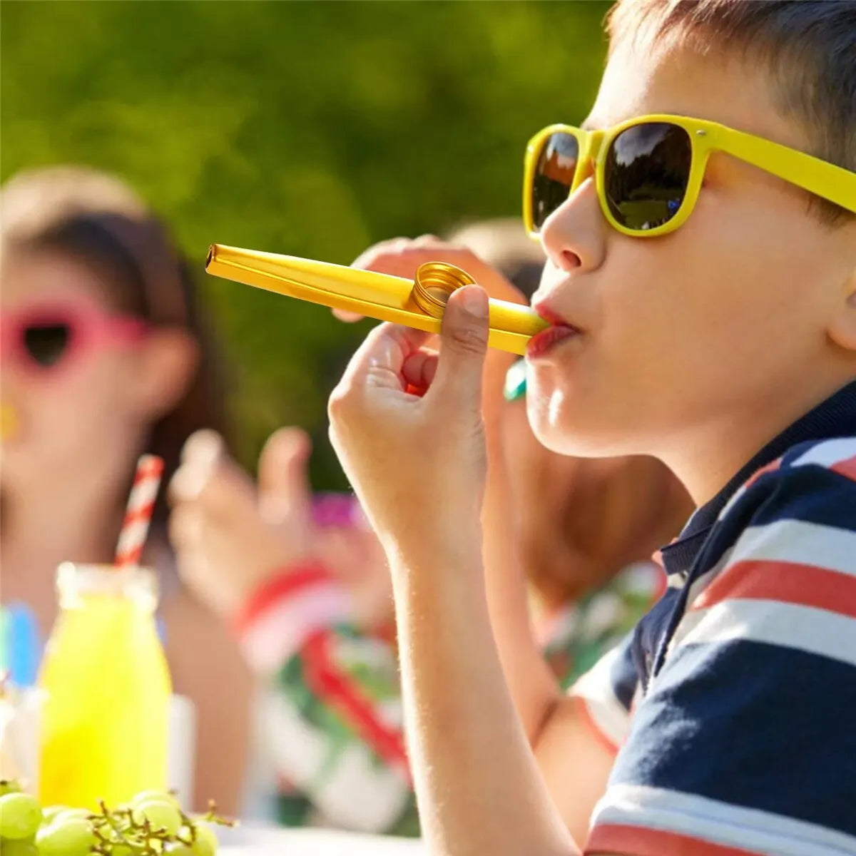 A young boy plays a yellow kazoo with a membrane diaphragm outdoors.