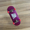 A purple skateboard featuring a wooden fingerboard and realistic red trucks resting on a wooden surface.