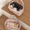 A pink quilted fabric storage basket filled with various bottles and a tissue paper item, resting on a wooden surface.