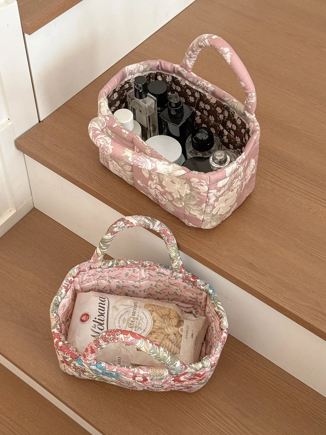 A pink quilted fabric storage basket filled with various bottles and a tissue paper item, resting on a wooden surface.