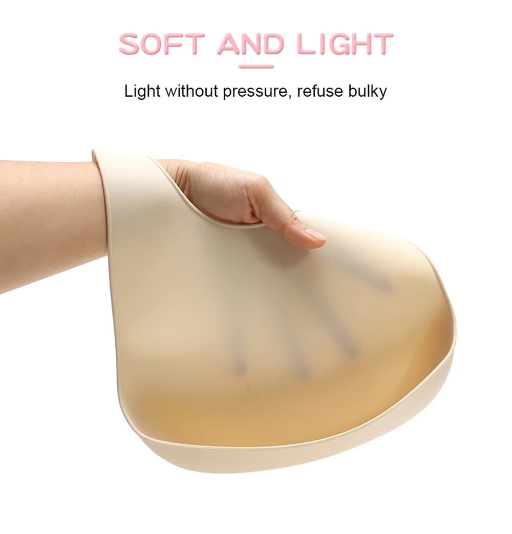 A hand is holding a light beige silicone baby bib with a catch pocket, demonstrating its soft and light design.