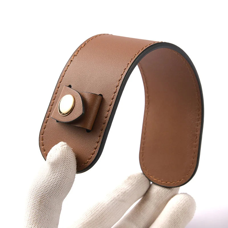 A brown genuine leather handbag handle wrap and shoulder pad being held by a hand.