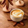 A ceramic bowl filled with orange-colored soup or puree is displayed on a wooden trivet set.