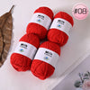 A pile of bright red Milk Cotton yarn skeins with white labels and a leaf in the background.