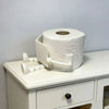 A white human-shaped freestanding toilet paper holder on a white cabinet.