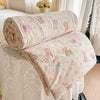 A light pink and cream quilted blanket featuring a pastoral print of small animals like rabbits and flowers.