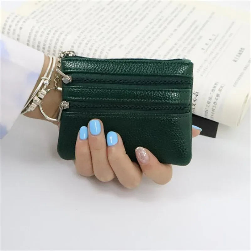 A hand holds a dark green compact PU leather two-zip coin purse against a white background.