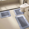 Three rectangular floor mats in shades of gray and blue are placed on a light floor near a toilet.