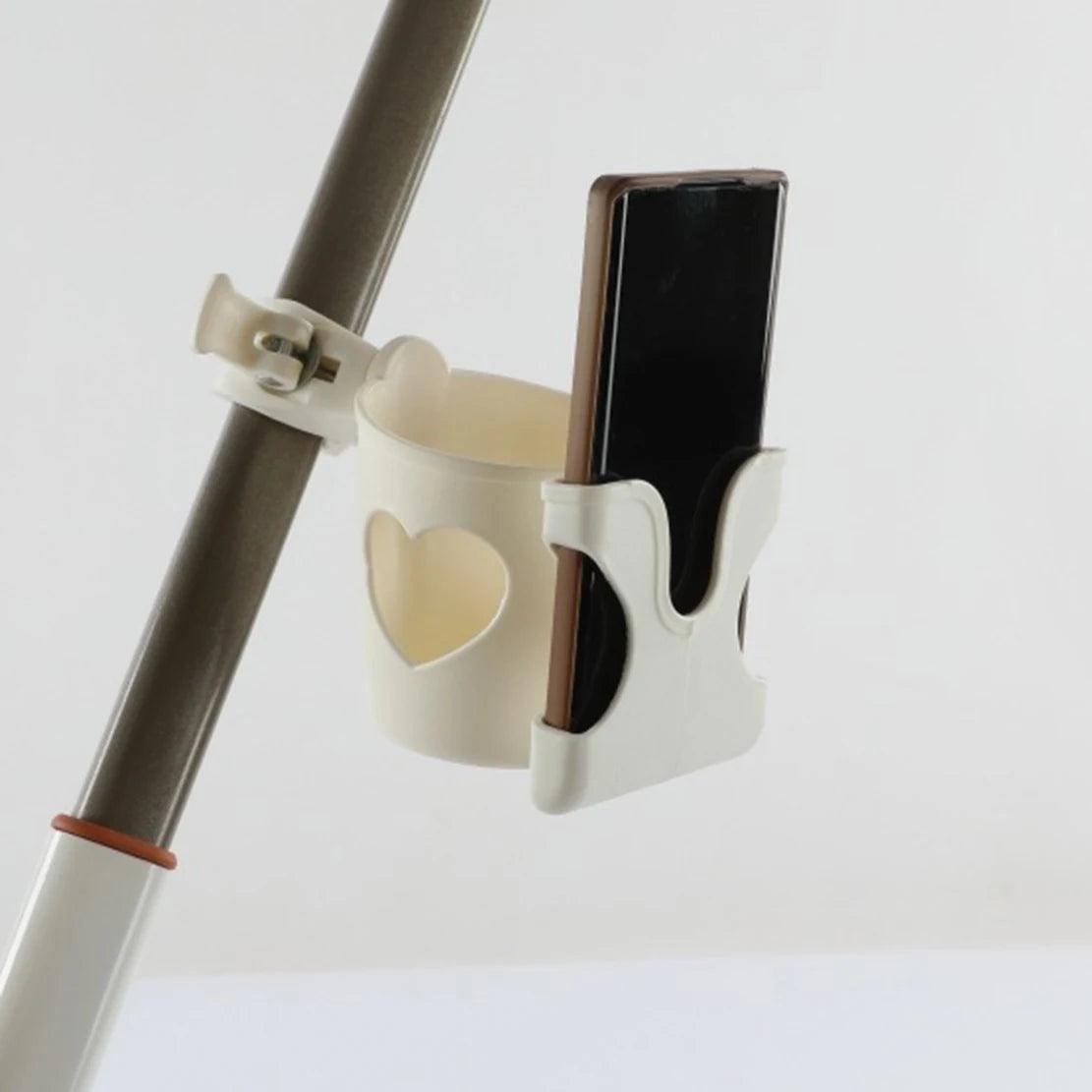 A white cup holder and phone mount attaches to a stroller bar, holding a smartphone.