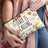 A beige makeup bag featuring an Italian theme with illustrations of landmarks and food, held by a person.
