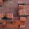 A close-up of a brick liner puller tool used to extract wire from a brick, set on reddish gravel.