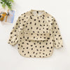 A beige long-sleeve smock for toddlers with a black polka dot pattern, shown flat lay.
