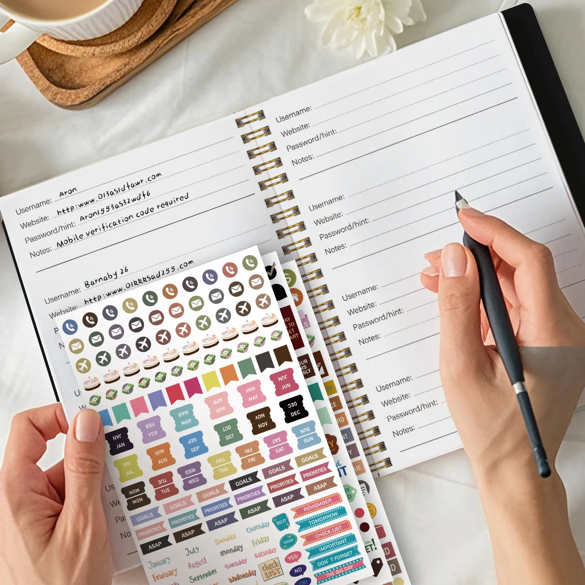 A hand is writing in an A5 weekly and monthly budget planner with stickers, showing various planning pages.