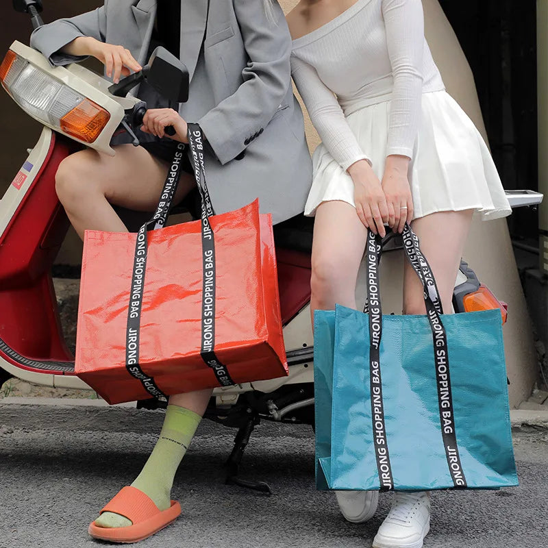 A woman wearing a gray blazer sits on a scooter while holding an orange shopping bag and another woman holds a blue shopping 