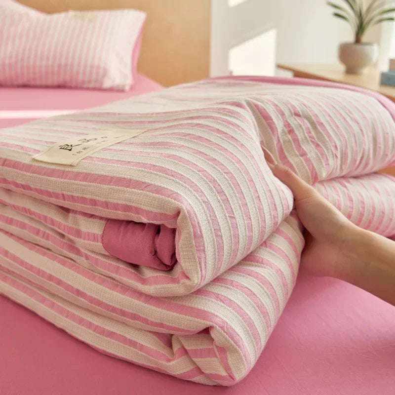 Pink and white striped breathable summer quilt rolled up on a pink surface.
