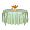 A round satin tablecloth in sage green with a vase of yellow flowers on top.