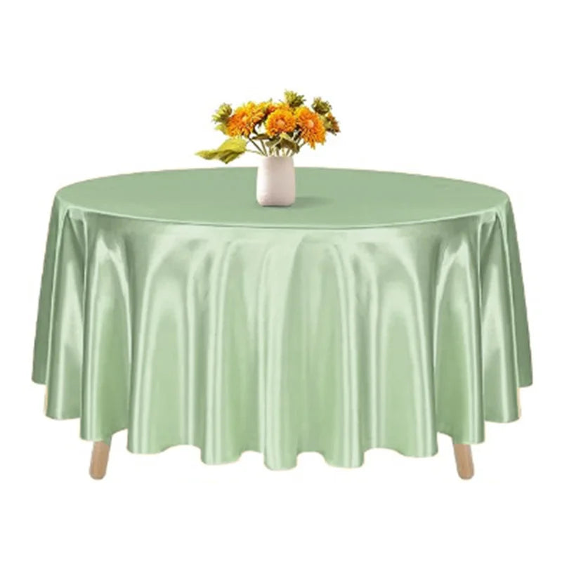 A round satin tablecloth in sage green with a vase of yellow flowers on top.