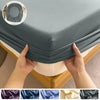 Hands are folding a fitted bed sheet with an elastic band onto a bed, showing various fabric colors.