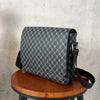 A dark gray patterned crossbody bag resting on a wooden stool.