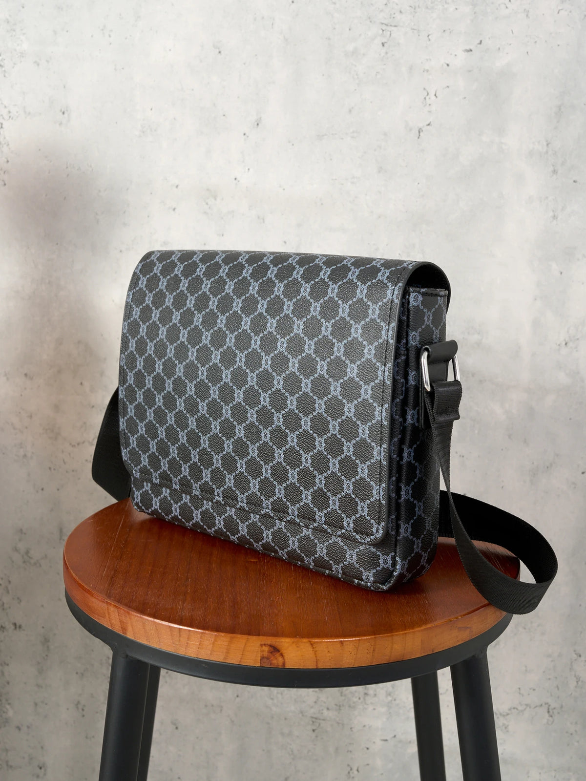 A dark gray patterned crossbody bag resting on a wooden stool.