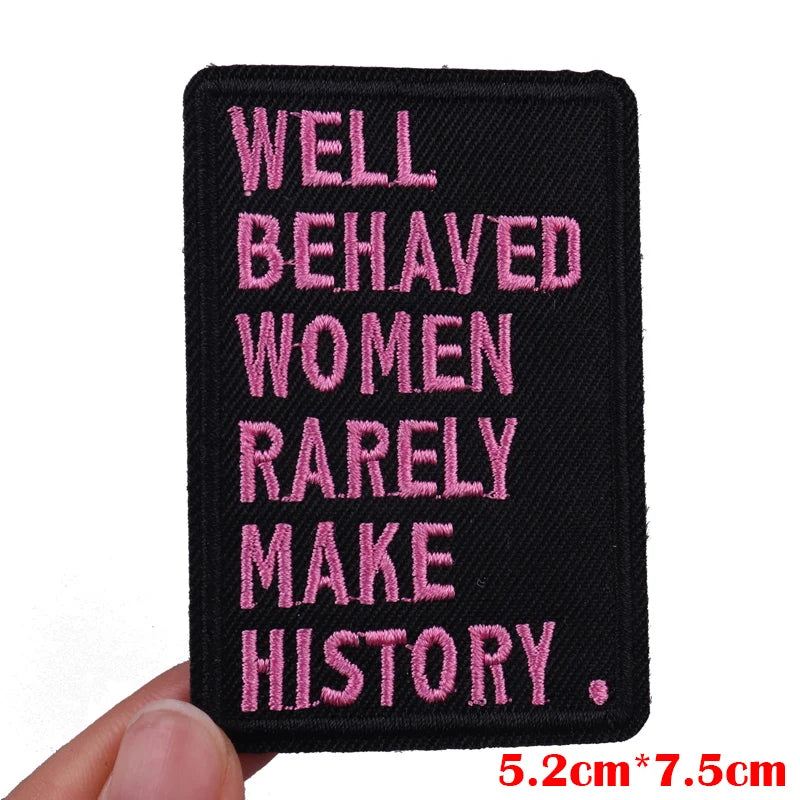 A black embroidered patch with pink text that reads Well Behaved Women Rarely Make History.